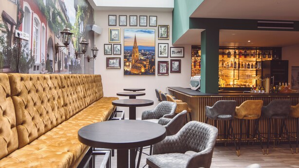 A modern lounge area with a plush sofa, round tables, and bar seating. - Hotel am Rathaus (Freiburg im Breisgau)