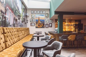 A modern lounge area with a plush sofa, round tables, and bar seating. - Hotel am Rathaus (Freiburg im Breisgau)