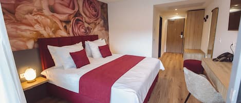 Una habitación de hotel con una cama grande, un escritorio, una silla y una pared con un mural floral.