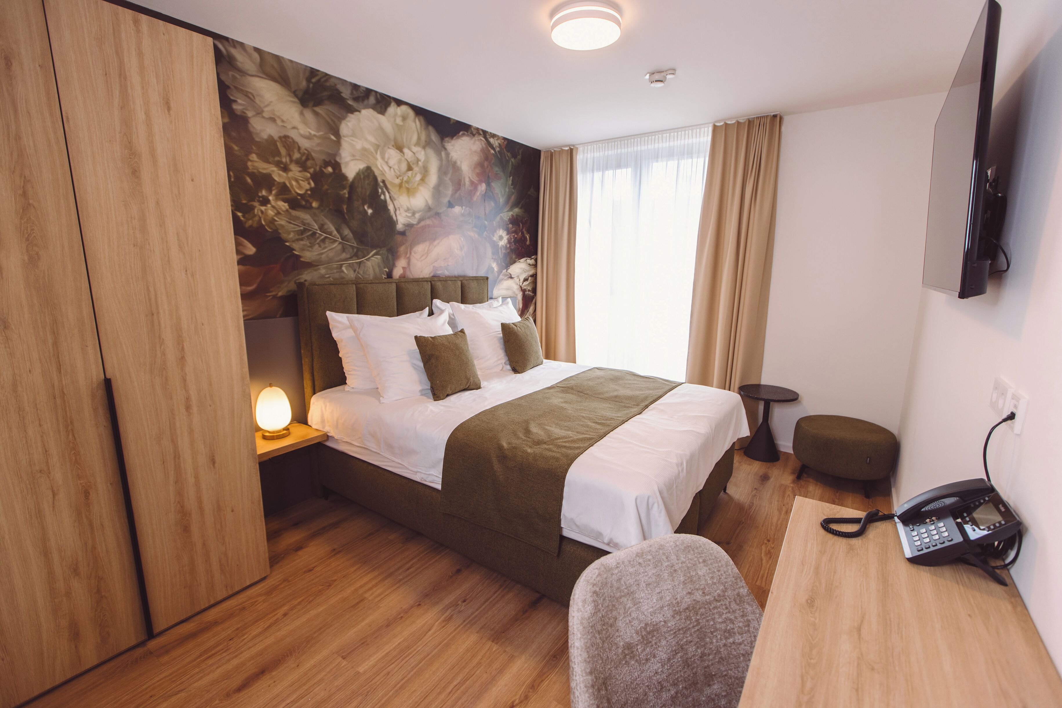 Une chambre d’hôtel avec un grand lit, un bureau avec un téléphone, une petite table et un téléviseur fixé au mur.