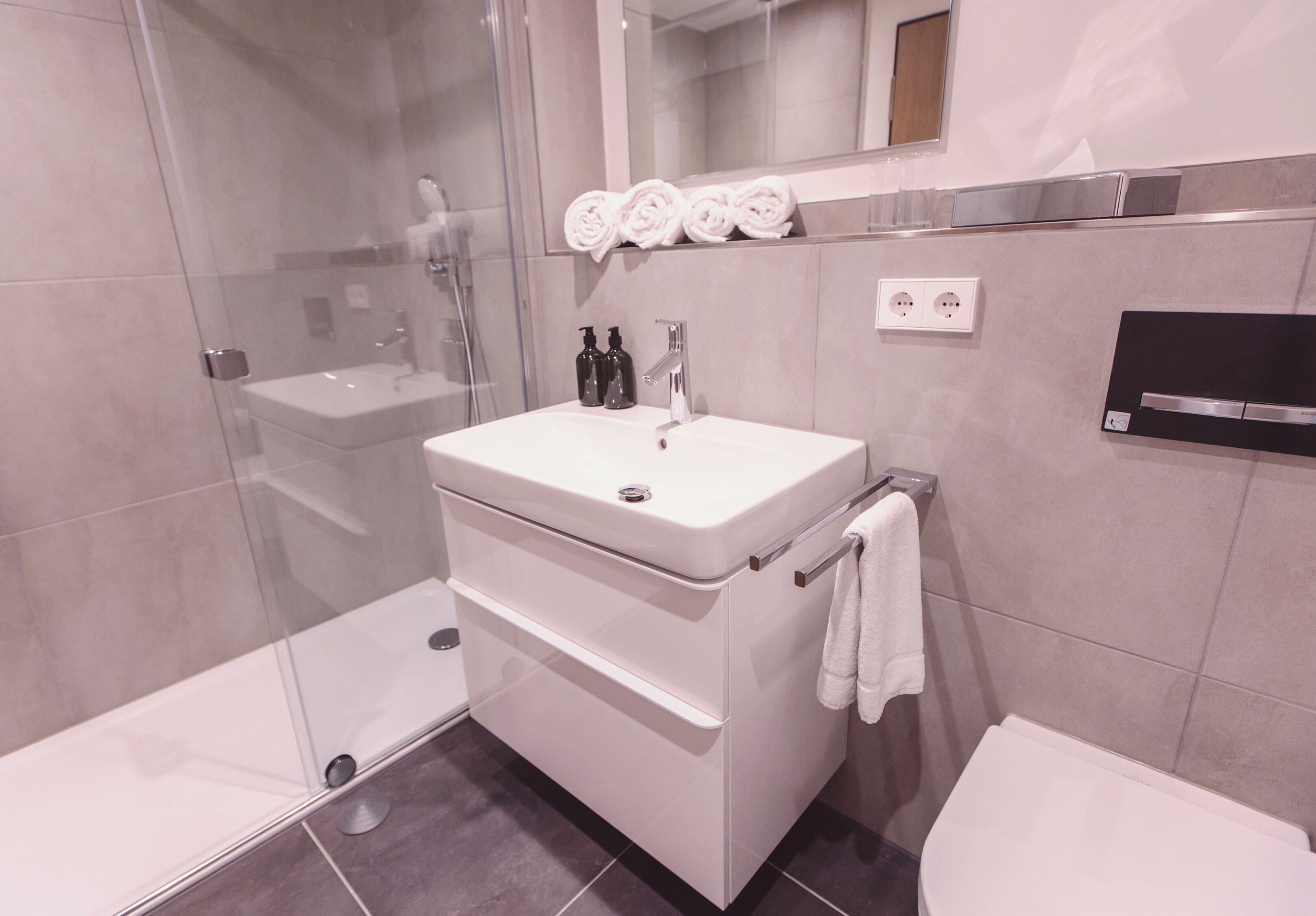 Ein modernes Badezimmer mit Duschkabine aus Glas, einem weißen Waschbecken und einer Toilette.