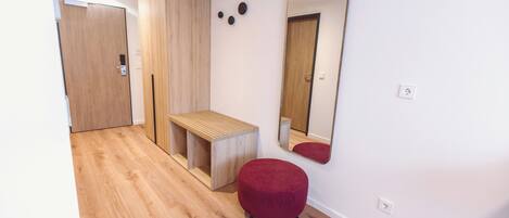 A modern room with a wooden bench, a red ottoman, a mirror, and a wardrobe.