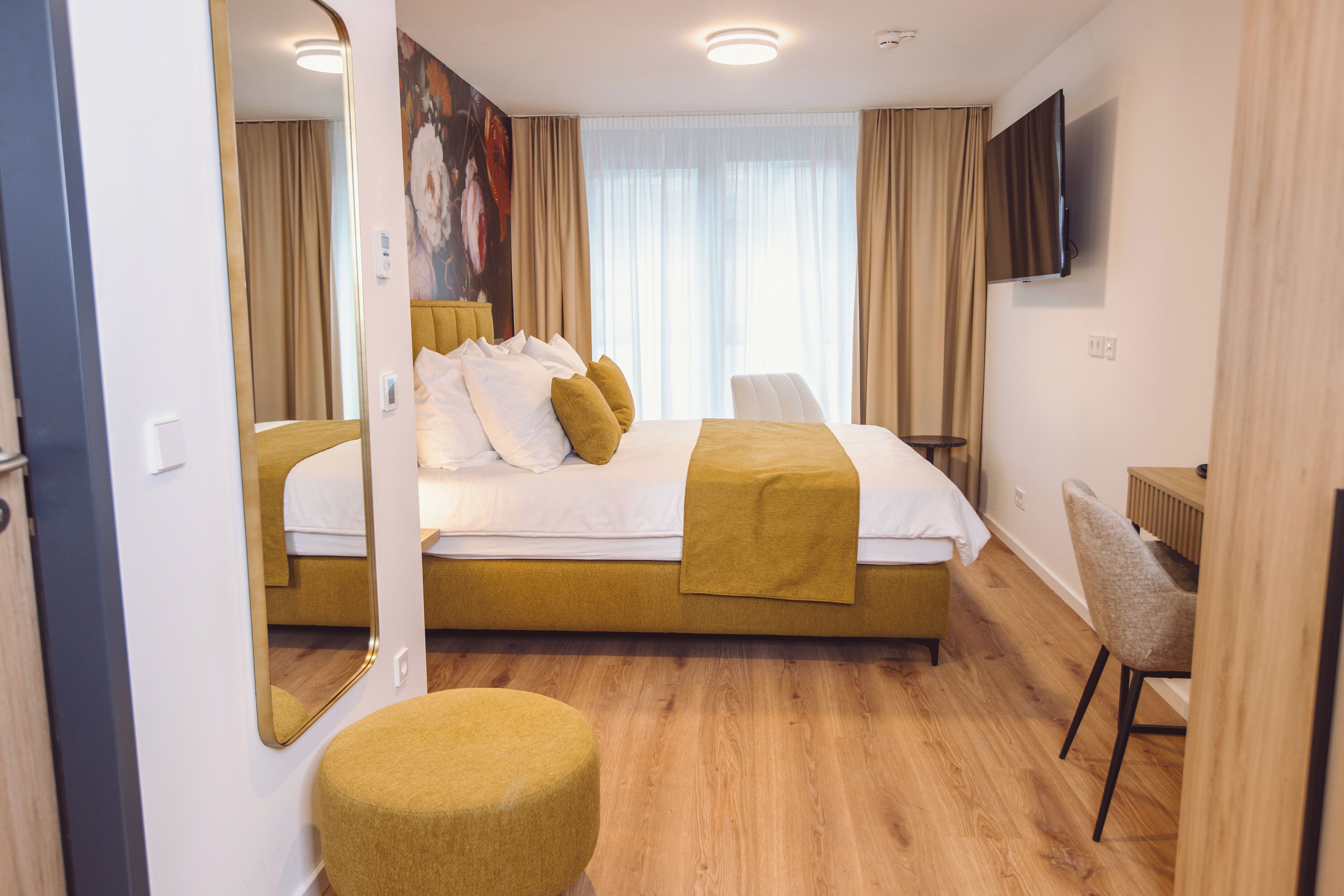 Ein modernes Hotelzimmer mit einem großen Bett, einer Sitzecke, einem Flachbildfernseher und einem großen Fenster mit Vorhängen.