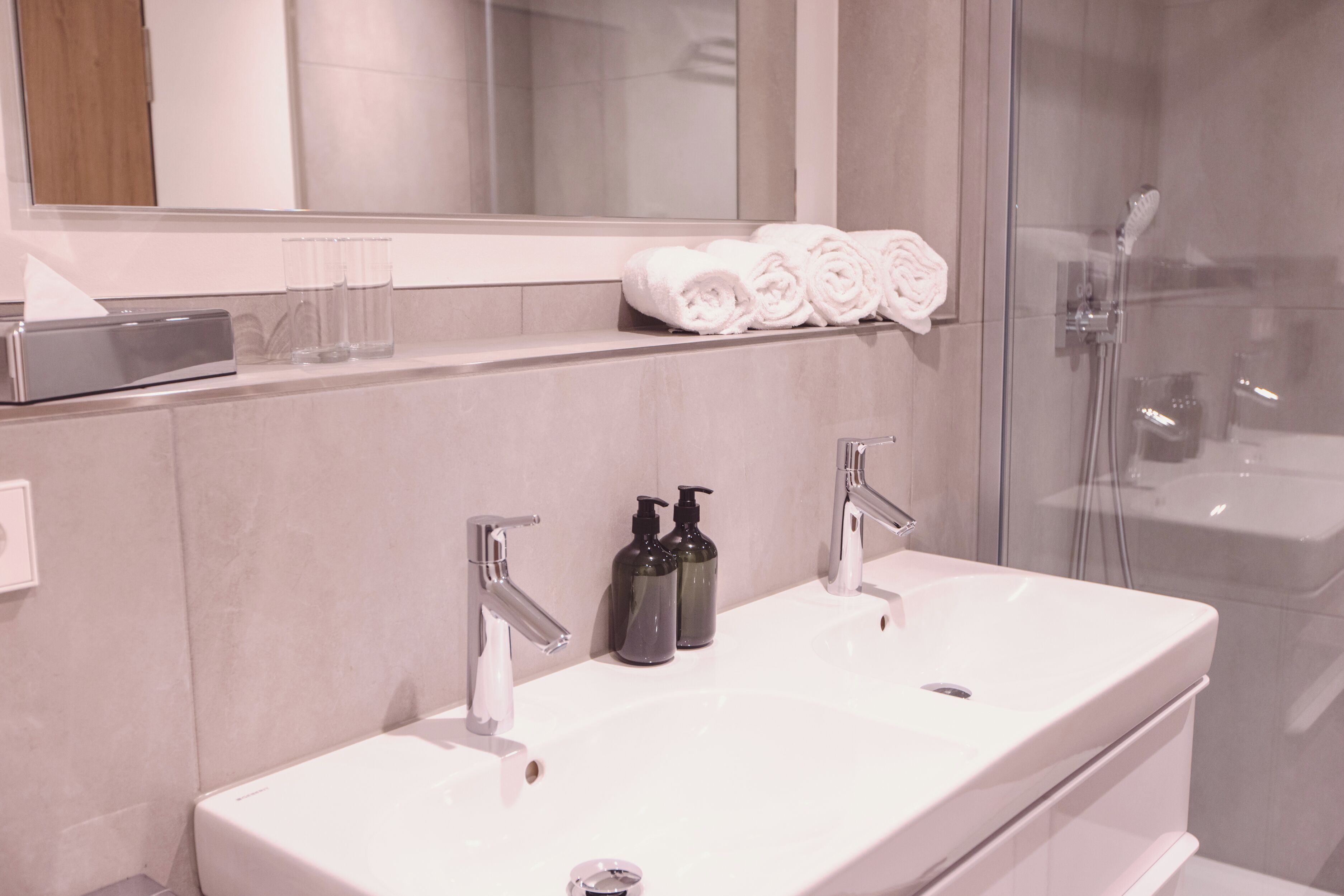 Ein modernes Badezimmer mit einem großen, weißen Waschbecken, zwei Wasserhähnen und einer Duschkabine aus Glas.