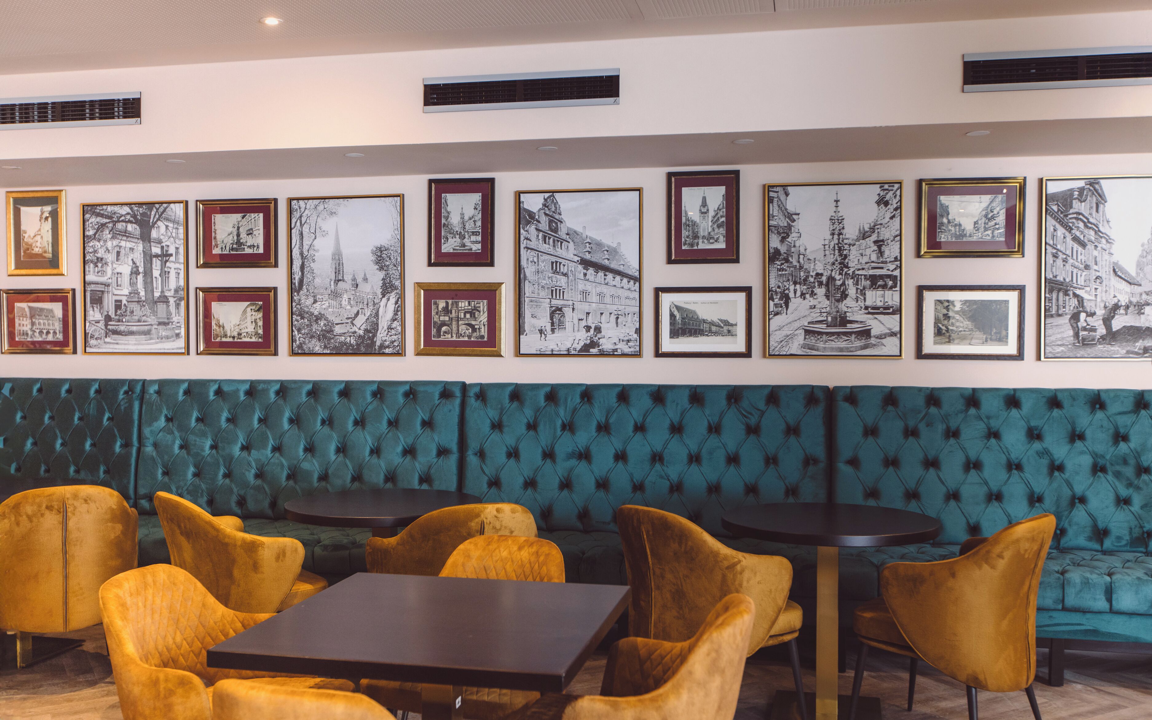 Un restaurant amb seients tapissats de color turquesa, cadires grogues i fotografies en blanc i negre emmarcades a la paret.