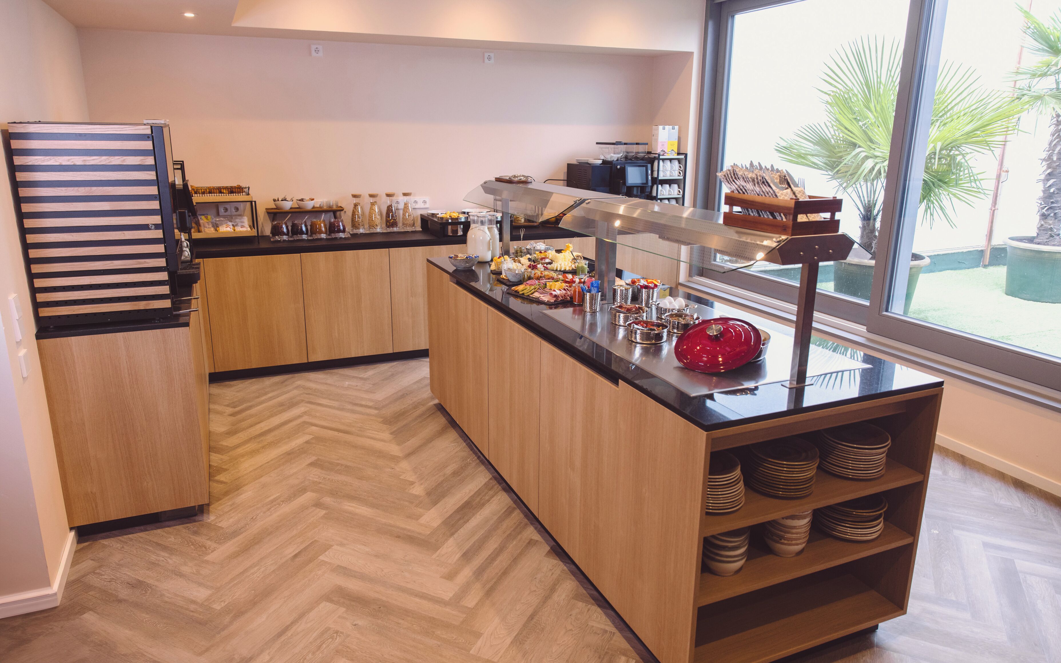 Una cocina moderna con suelo de madera en espiga, un mostrador buffet con diferentes comidas y un ventanal con vistas a zonas verdes.