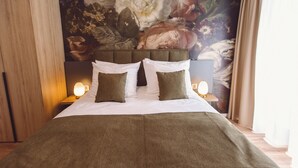 A neatly made bed with a green blanket and pillows, a wooden headboard, and a floral mural on the wall behind. - Hotel am Rathaus (Freiburg im Breisgau)
