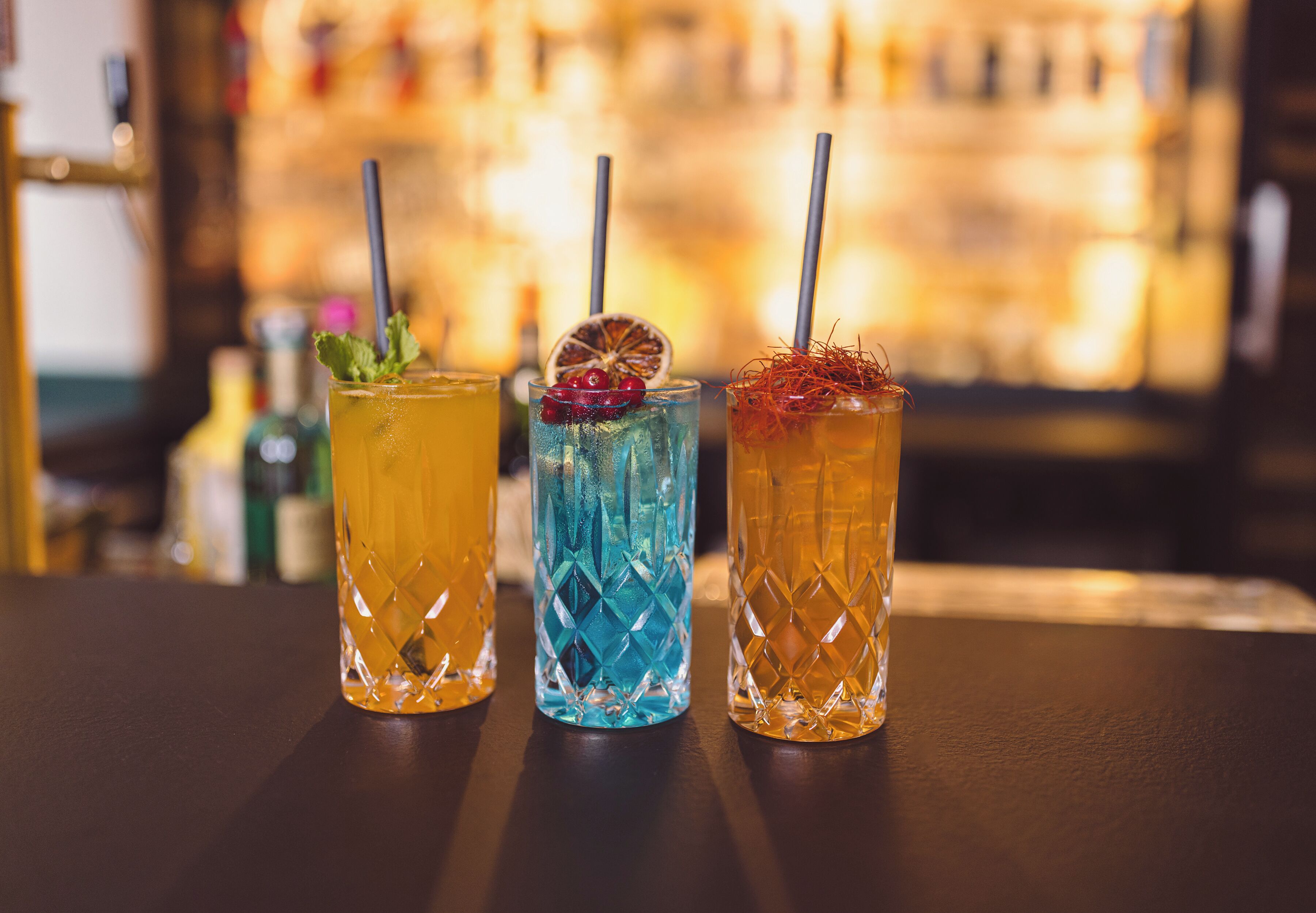 Three drinks with straws on a bar counter.
