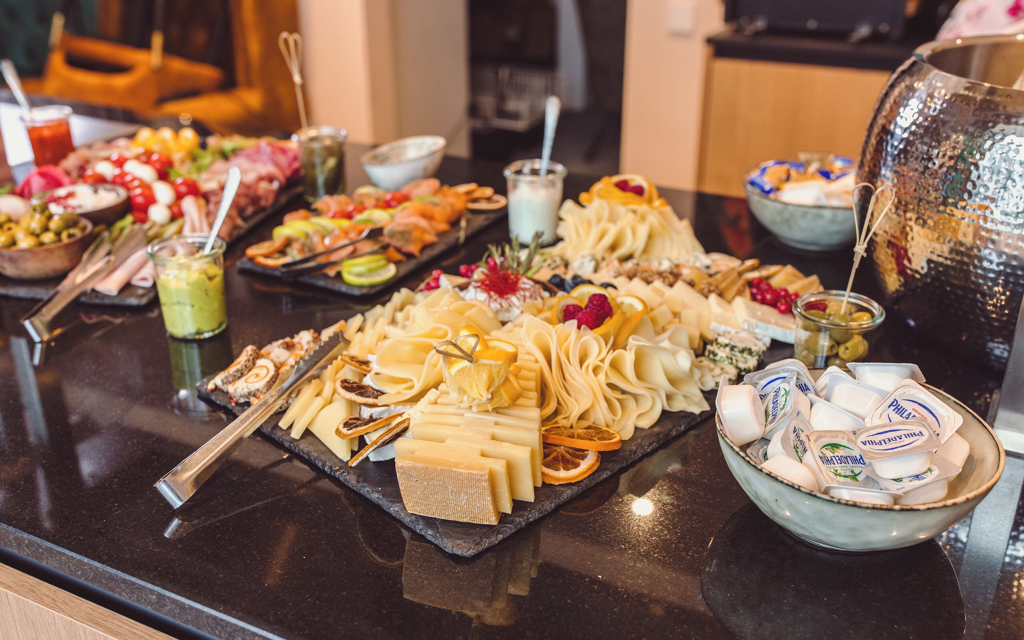 A buffet with various cheeses, fruits, and condiments.