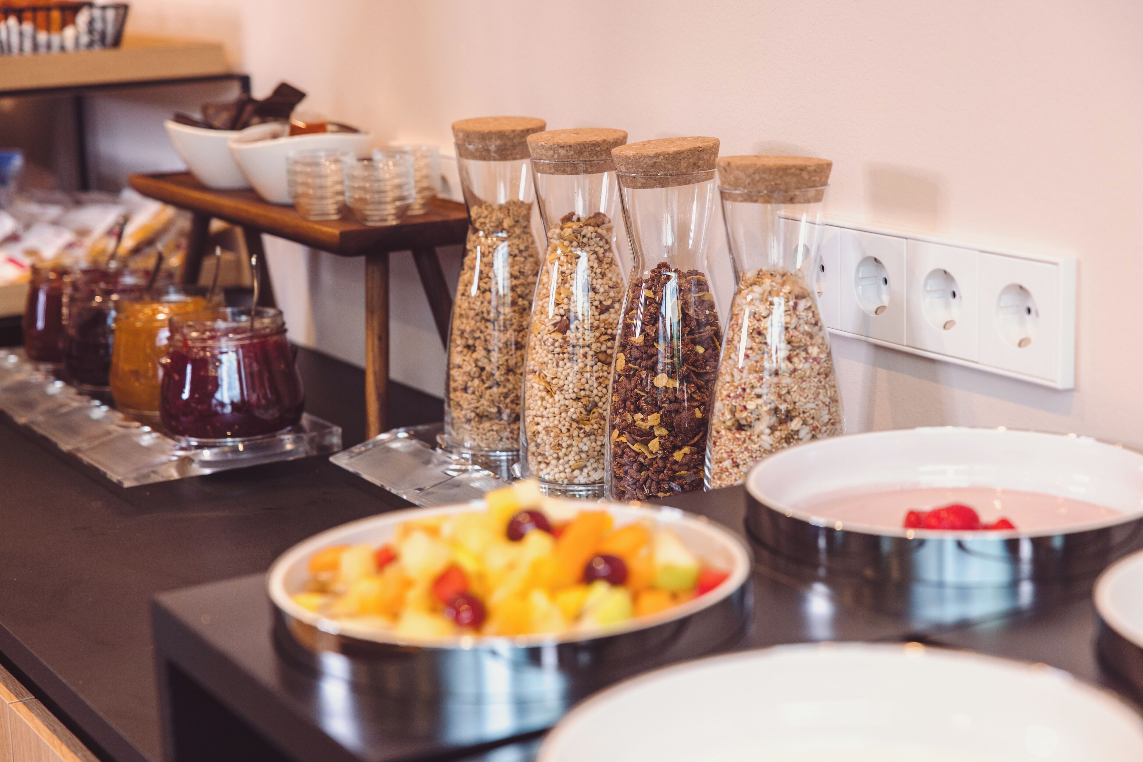 Un bufé con diversos alimentos y recipientes, incluyendo frascos de conservas y cuencos de fruta.