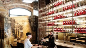 A bar area with a bartender serving a customer, bar stools, and shelves with bottles.