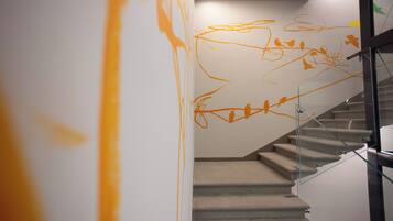 Una scala con ringhiera in vetro, un muro con graffiti arancioni astratti e un moderno apparecchio di illuminazione.