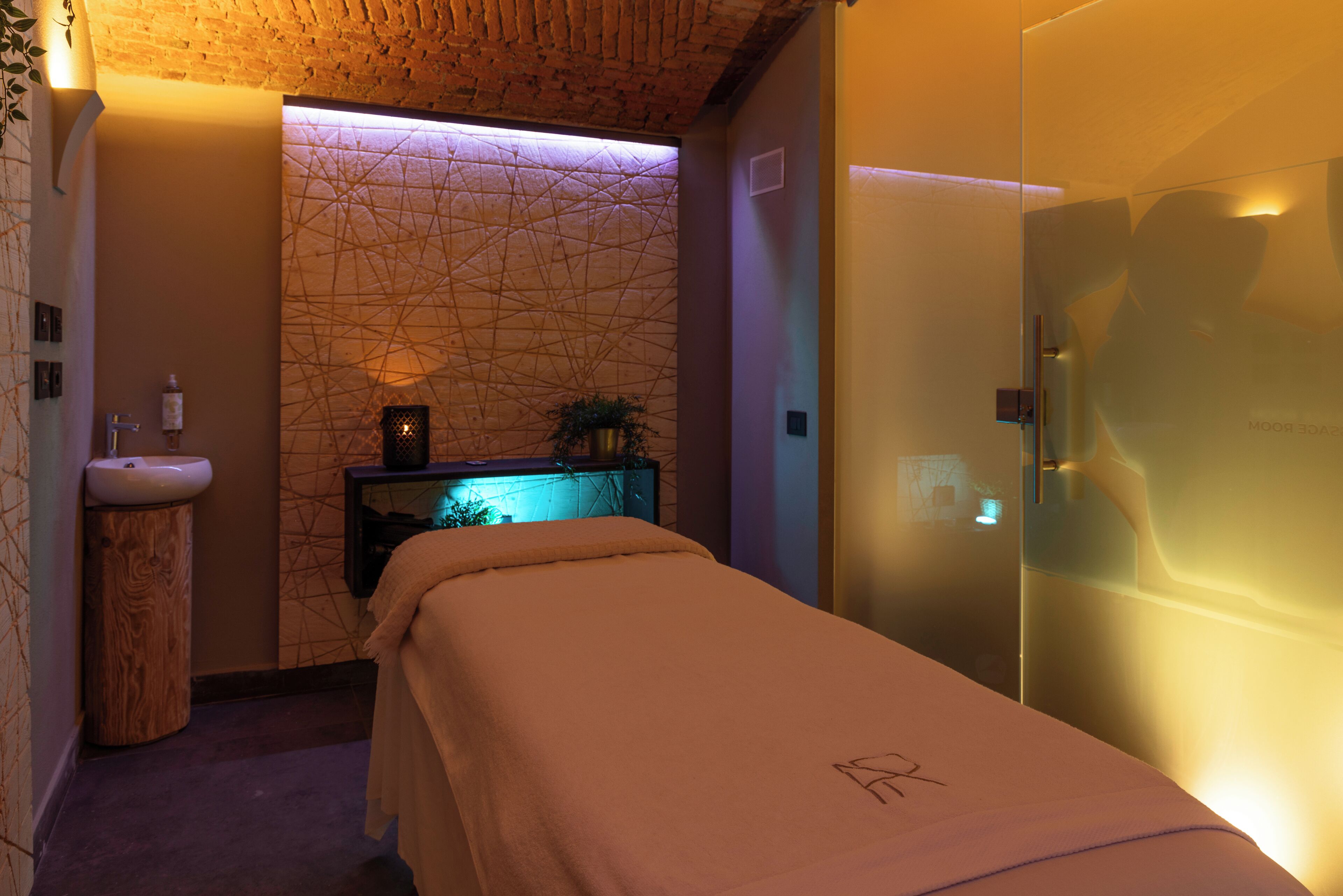 A spa room with a massage table, a sink, and a glass shower enclosure.