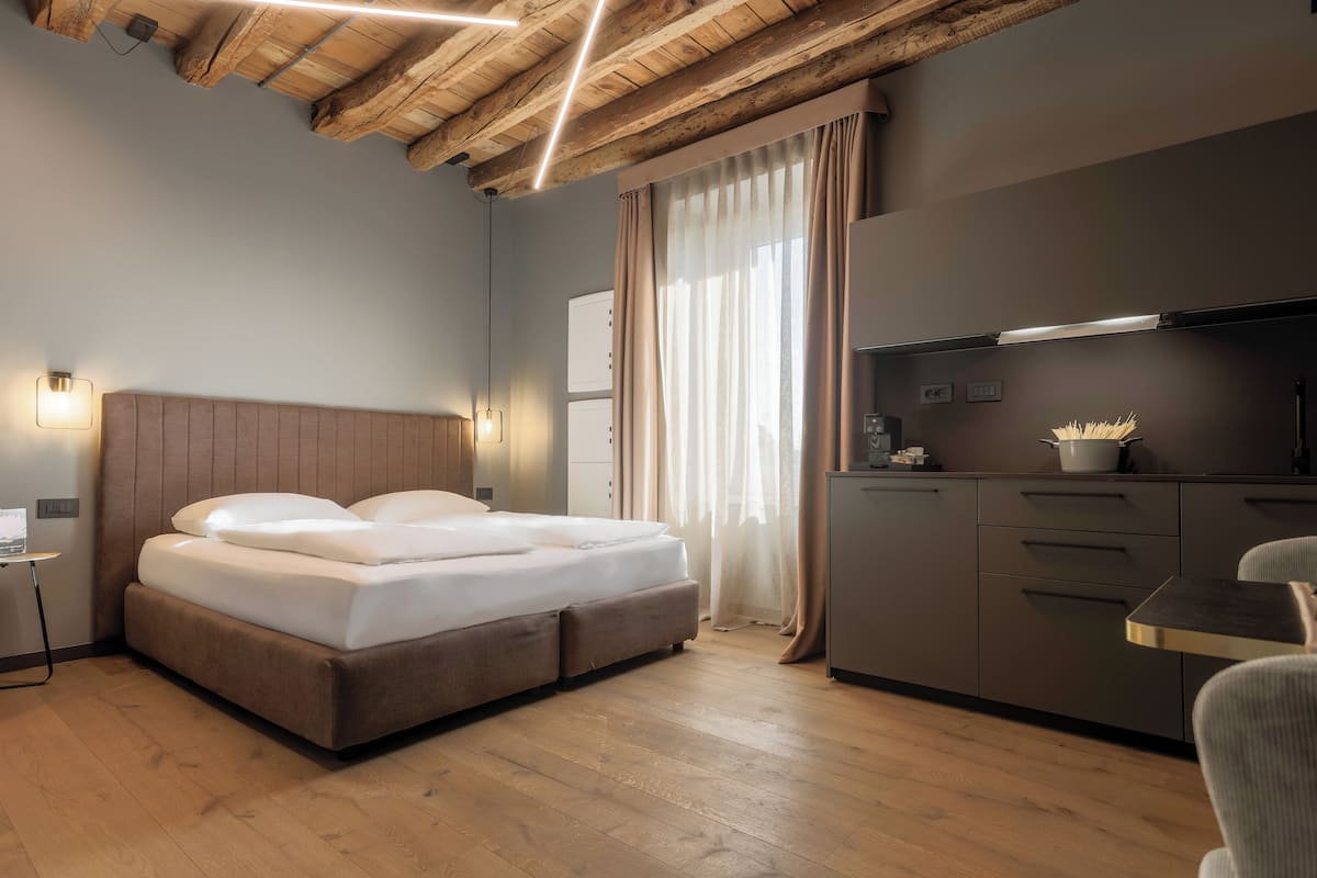 Moderni hotellihuone, jossa on puinen katto, valkoisilla lakanoilla varustettu sänky, pieni työpöytä lampun kanssa sekä minikeittiö, jossa on mikroaaltouuni.