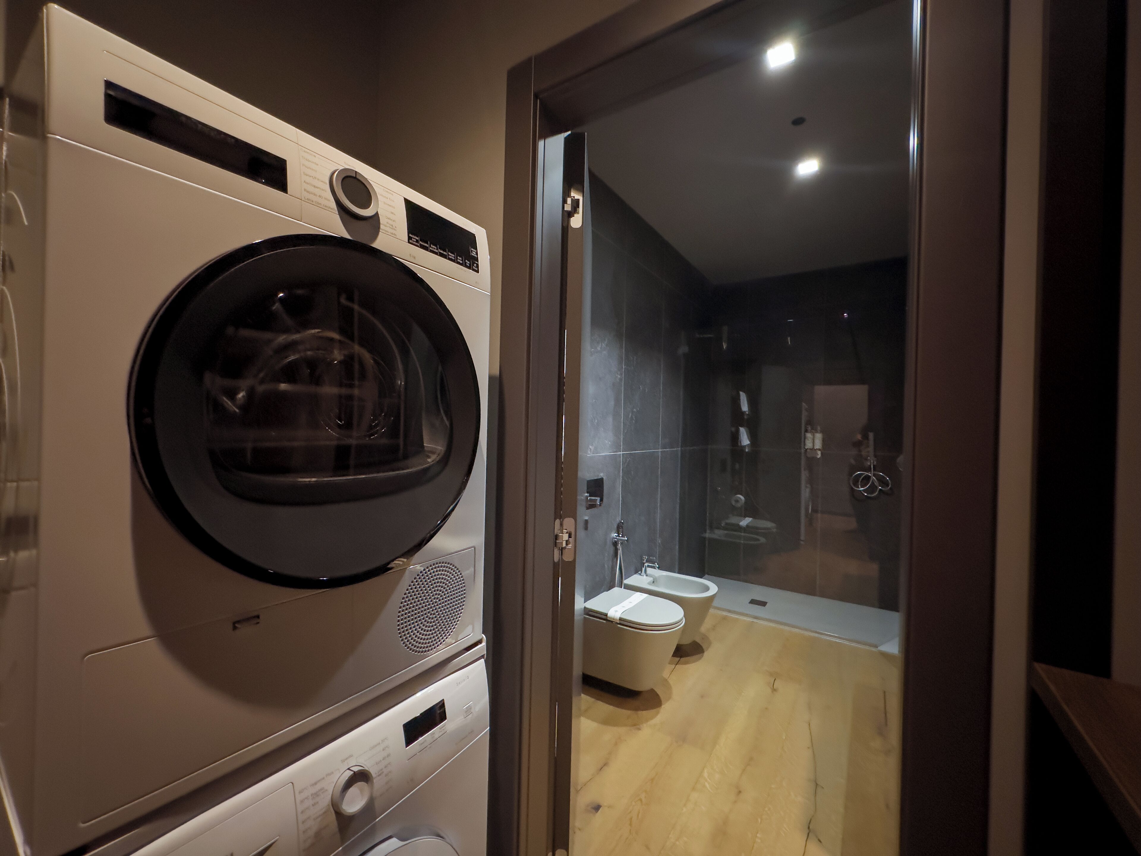 A compact bathroom with a washing machine, a toilet, and a glass-enclosed shower area.