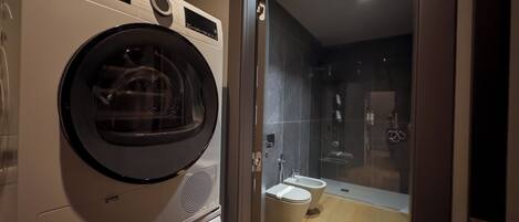 A compact bathroom with a washing machine, a toilet, and a glass-enclosed shower area.