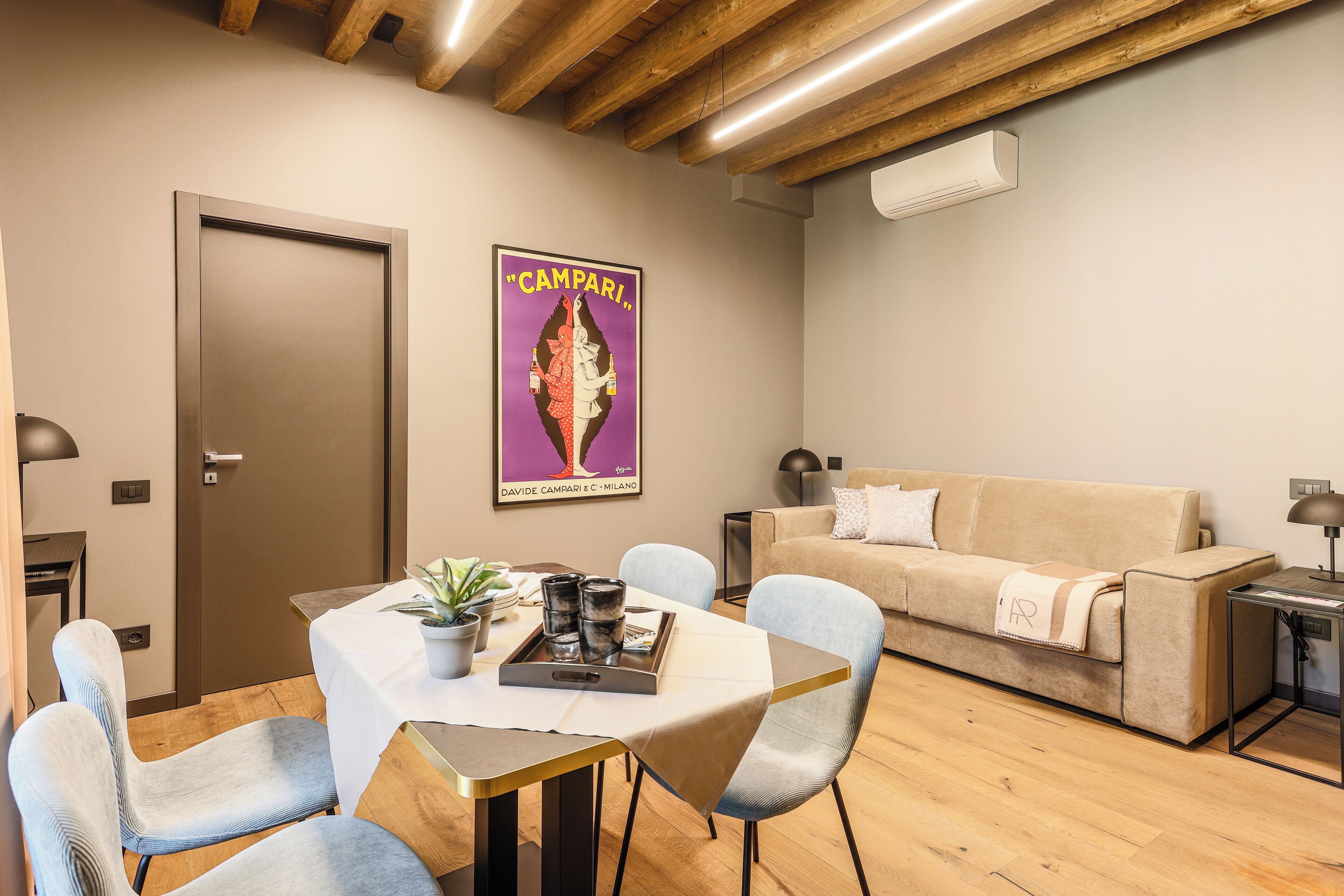 Een moderne woonkamer met een houten plafond, een beige bank, een eettafel met stoelen en een poster aan de muur.