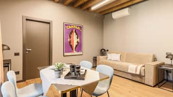 Een moderne woonkamer met een houten plafond, een beige bank, een eettafel met stoelen en een poster aan de muur.