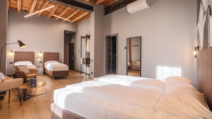 A modern hotel room with two beds, a sitting area with a chair and table, wooden ceiling beams, and a large mirror.
