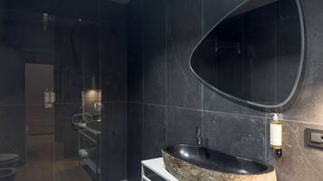 A modern bathroom with a large oval mirror, a stone sink, and a glass shower enclosure.