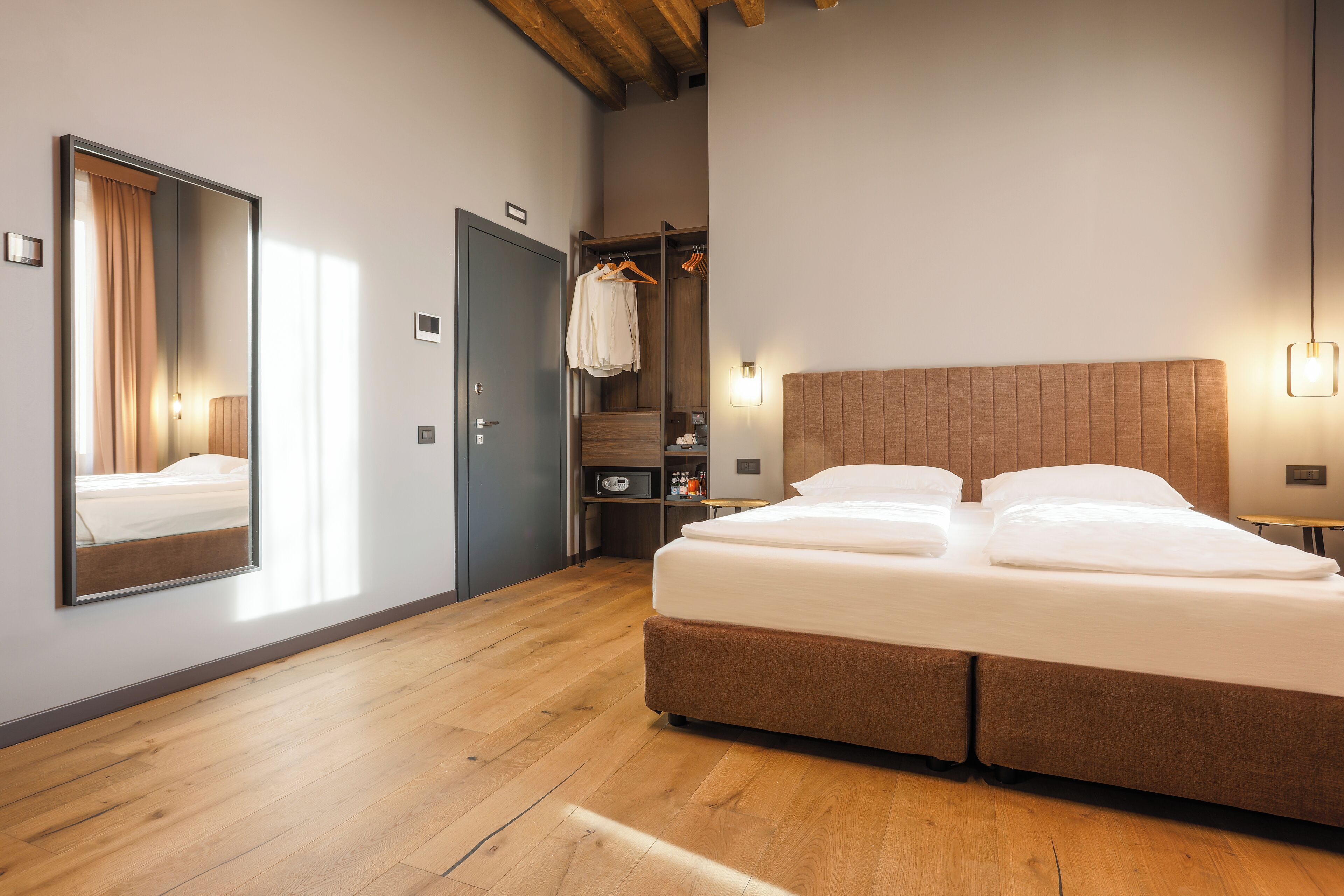 A modern bedroom with a large bed, a wardrobe, a mirror, and a small desk area.