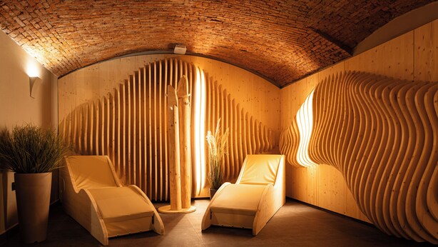 A spa room with two reclining chairs, a wooden wall with vertical slats, and a brick ceiling.