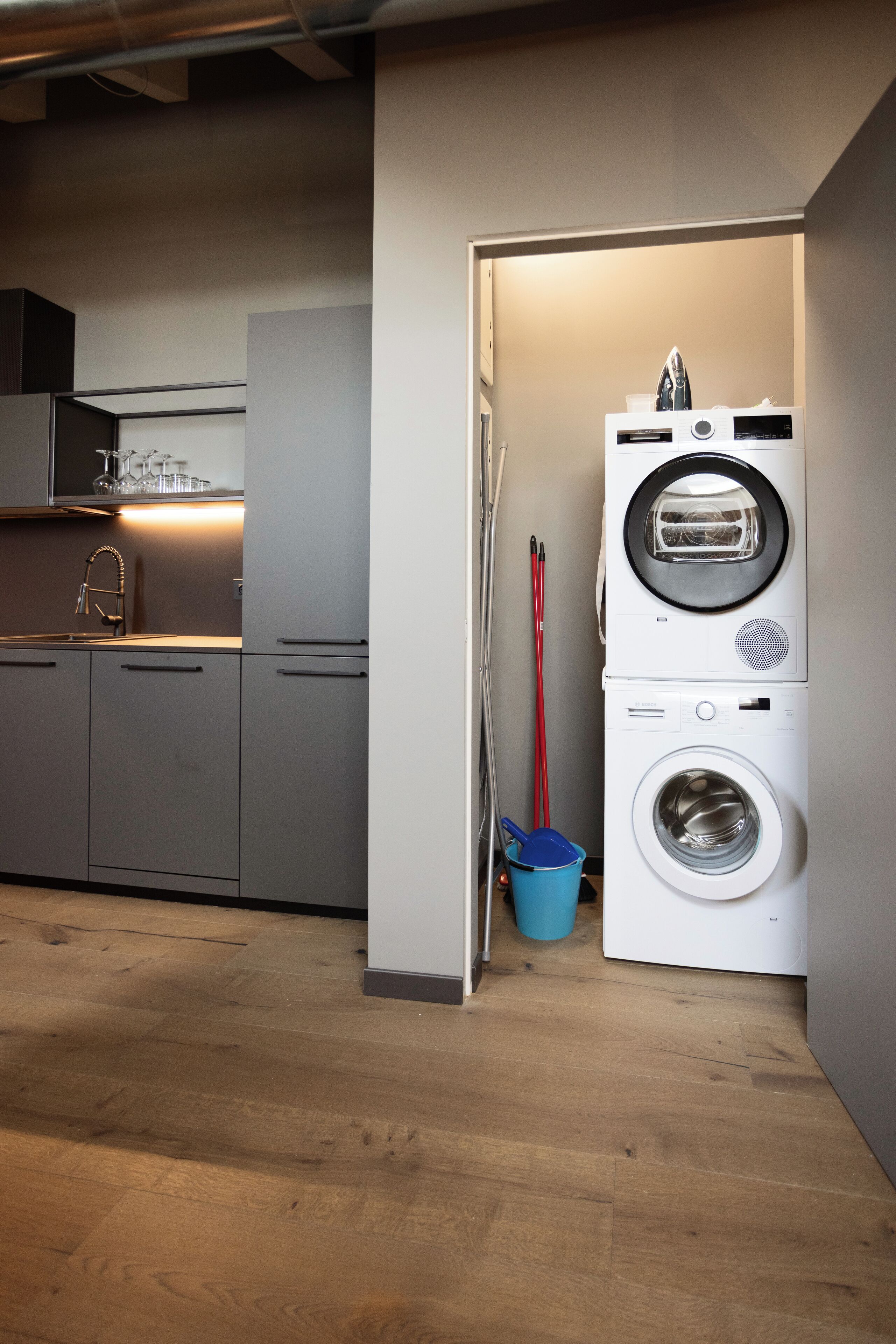 A compact kitchen with modern appliances, including a washing machine and dryer, and a blue bucket near the entrance.