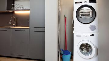 A compact kitchen with modern appliances, including a washing machine and dryer, and a blue bucket near the entrance.