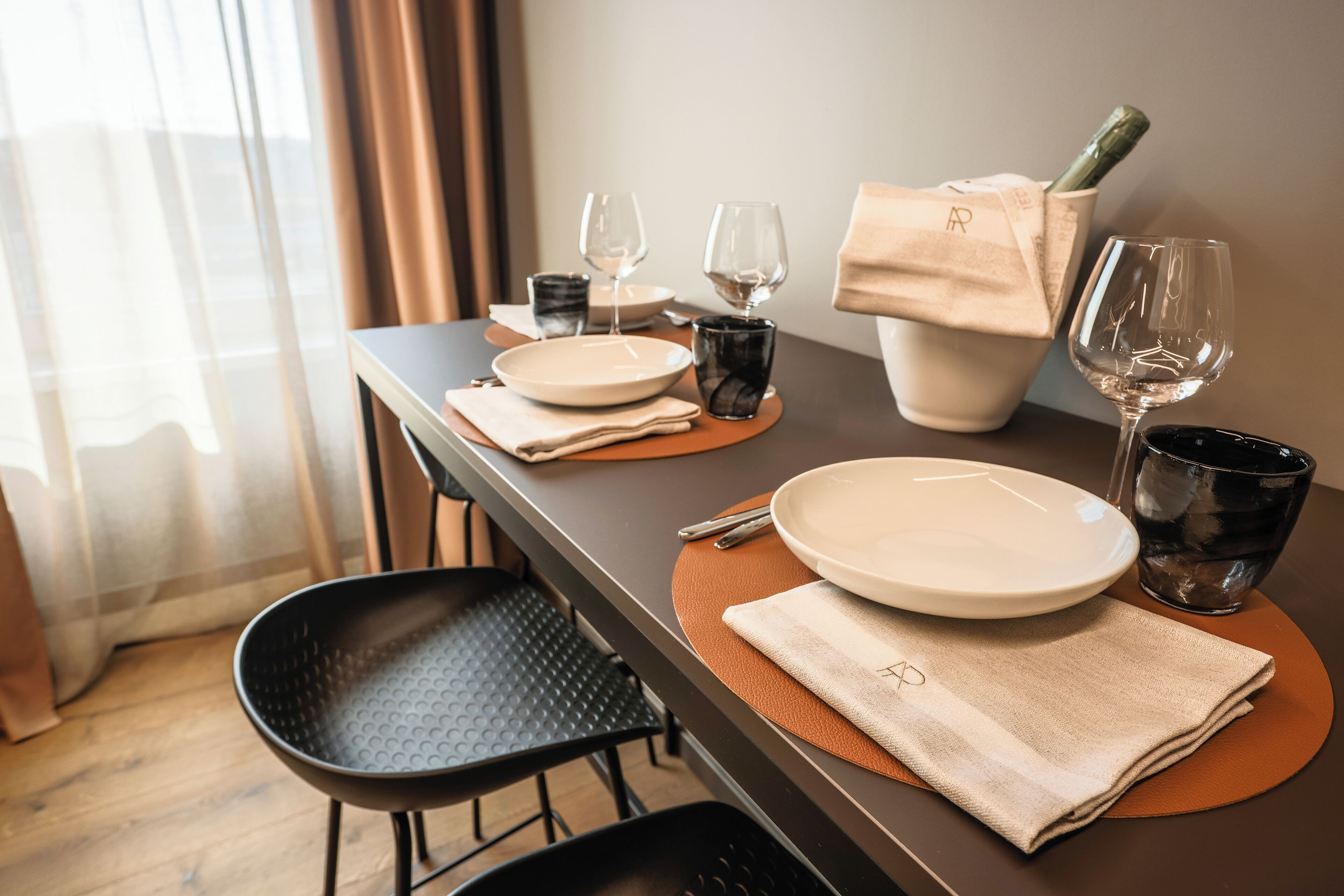 A neatly set dining table with plates, glasses, and a bottle of champagne, indicating a dining area in a hotel room.