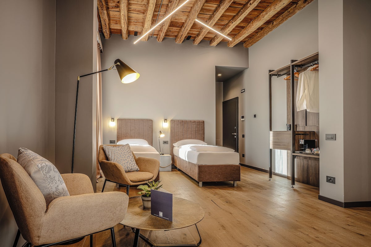 Moderni hotellihuone, jossa on kaksi sänkyä, sohva, ruokapöytä ja pieni keittiönurkkaus.