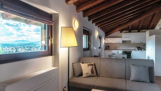 A modern living room with a sofa, a lamp, and a view of a cityscape through a window. - Loft Venere (Como)