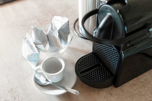 Una cafetera, una taza de café y un bol de vidrio con papel arrugado sobre una encimera.