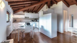 A modern kitchen with white cabinets, a dining area with a table and chairs, and a wooden ceiling. - Loft Venere (Como)