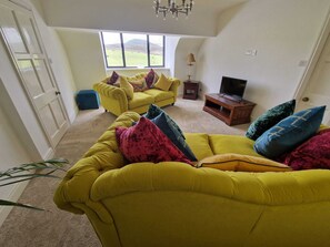 A living room with two yellow sofas, a TV stand, and a window with a view of the countryside. - Luxury Penthouse Apartment - Beautiful Countryside (Macclesfield)