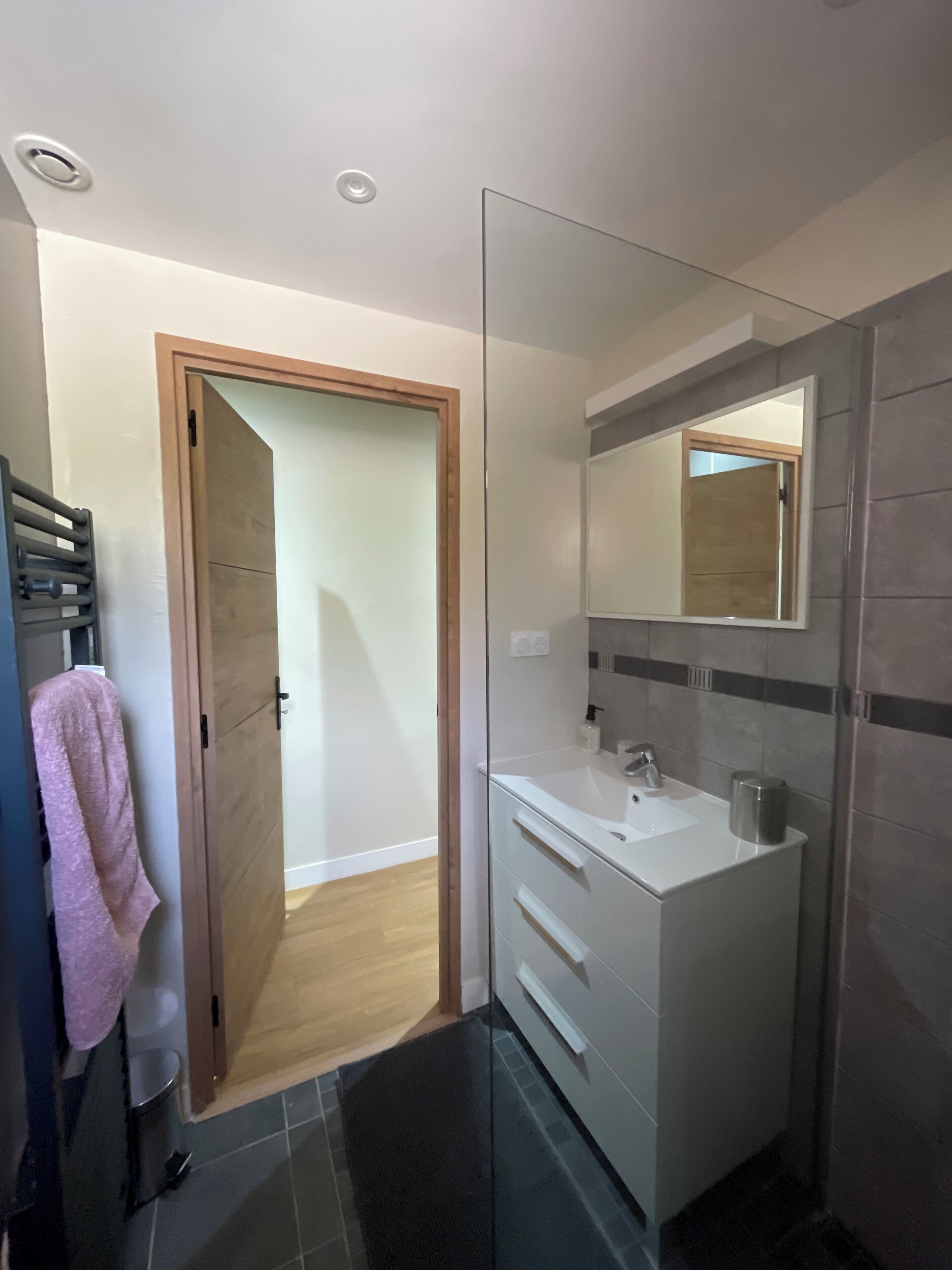Un baño moderno con cabina de ducha de vidrio, un lavabo blanco y un espejo grande.