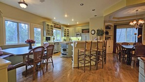 A spacious kitchen with wooden flooring, a central island with seating, and a dining area with a chandelier. - 7 Titleist-Sunriver, Oregon: Woodlands Golf Course View, Air Conditioning, SHARC Aquatics, BBQ, WiFi, Mt. Bachelor, Deschutes River, Tennis, Bike Paths (Sunriver)