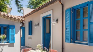 A dining area with a table set for four, surrounded by red chairs, in a building with blue shutters and a tiled roof. - Villa Plaka 3BR 9ppl Private Yard, 200m from Acropolis Metro&Museum (Athina)