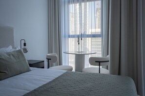 A hotel room with a bed, a small table, two chairs, a nightstand, and a window with curtains. - Waves - Comfort and Style in a 21st-Floor Studio With View (Dubai)