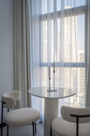 A modern room with a round table and two chairs, large windows with sheer curtains, and a view of city buildings. - Waves - Comfort and Style in a 21st-Floor Studio With View (Dubai)