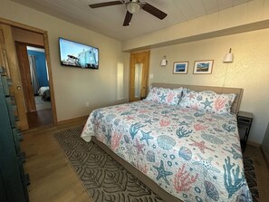 Un dormitorio con una cama, un televisor en la pared y una puerta que da a otra habitación.
