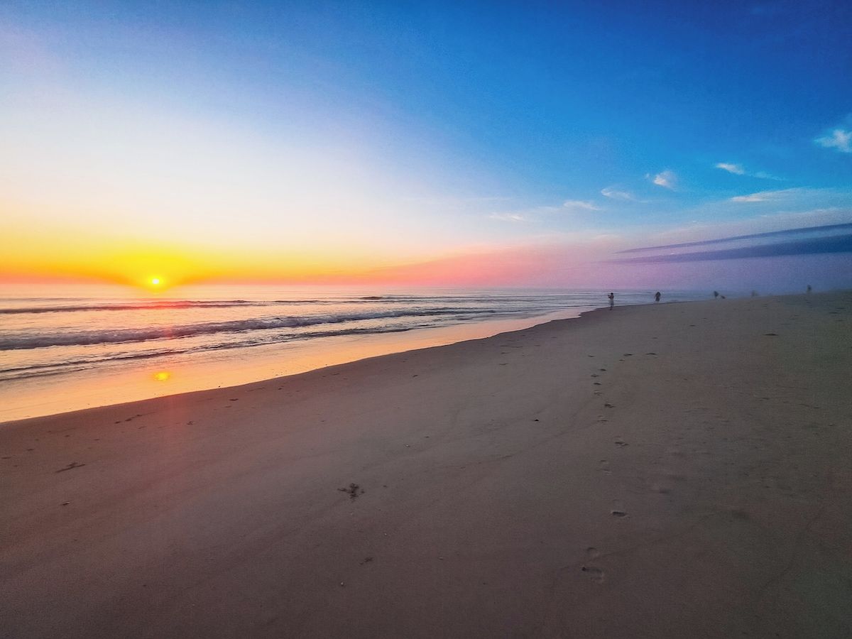 Une plage au coucher du soleil, un ciel dégagé et des empreintes de pas dans le sable.