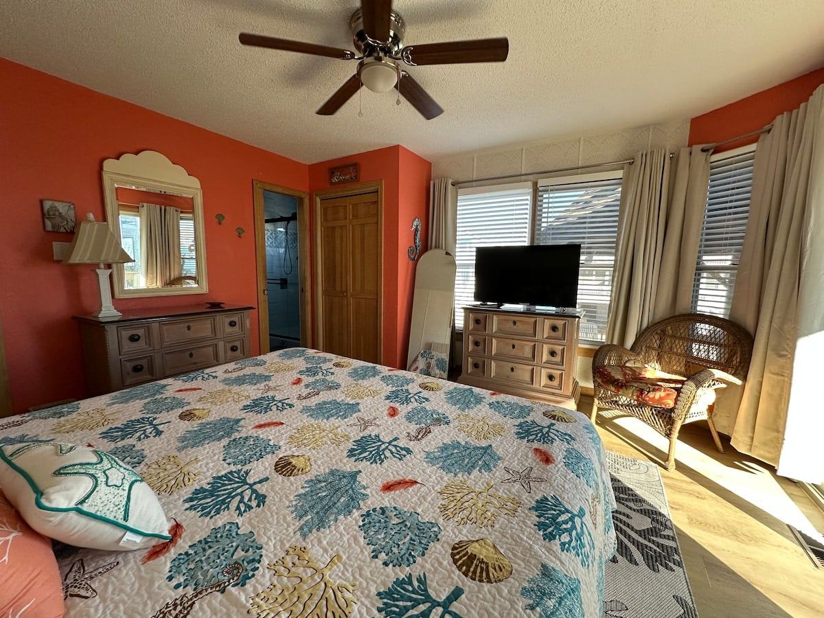A bedroom with a bed, dresser, television, and a chair.