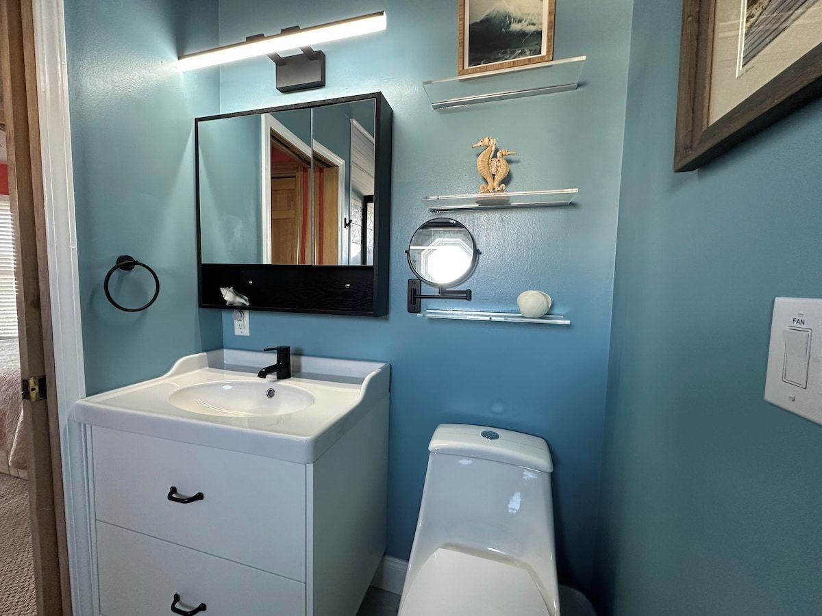 A bathroom with a white sink, a mirror, a toilet, and a shelf with a decorative item.
