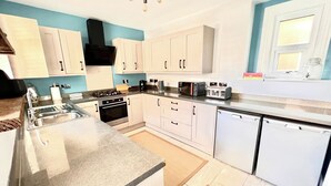 A modern kitchen with white cabinets, a built-in oven, a dishwasher, and a countertop with various appliances. - Seaside Haven at Willowdene Cottage (Llandudno)