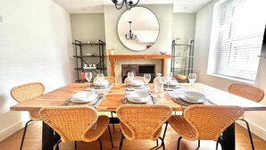 A dining room with a large wooden table set for six, surrounded by wicker chairs. - Seaside Haven at Willowdene Cottage (Llandudno)