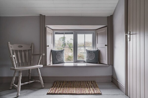 Una habitación con ventanal, una mecedora y un tapiz estampado.