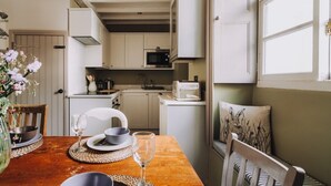 A compact kitchen with white cabinets, a microwave, and a toaster. There is a dining table with a vase of flowers and a glass of wine.