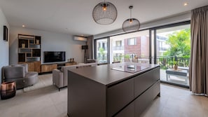 Una sala de estar moderna con una isla central grande, un televisor de pantalla plana y un balcón con vistas a la ciudad.
