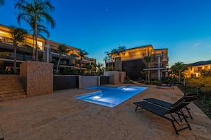 Un hotel con piscina, sillas de descanso y un área exterior bien iluminada.