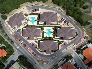 An aerial view of a residential area with multiple houses, a swimming pool, and a curved road.